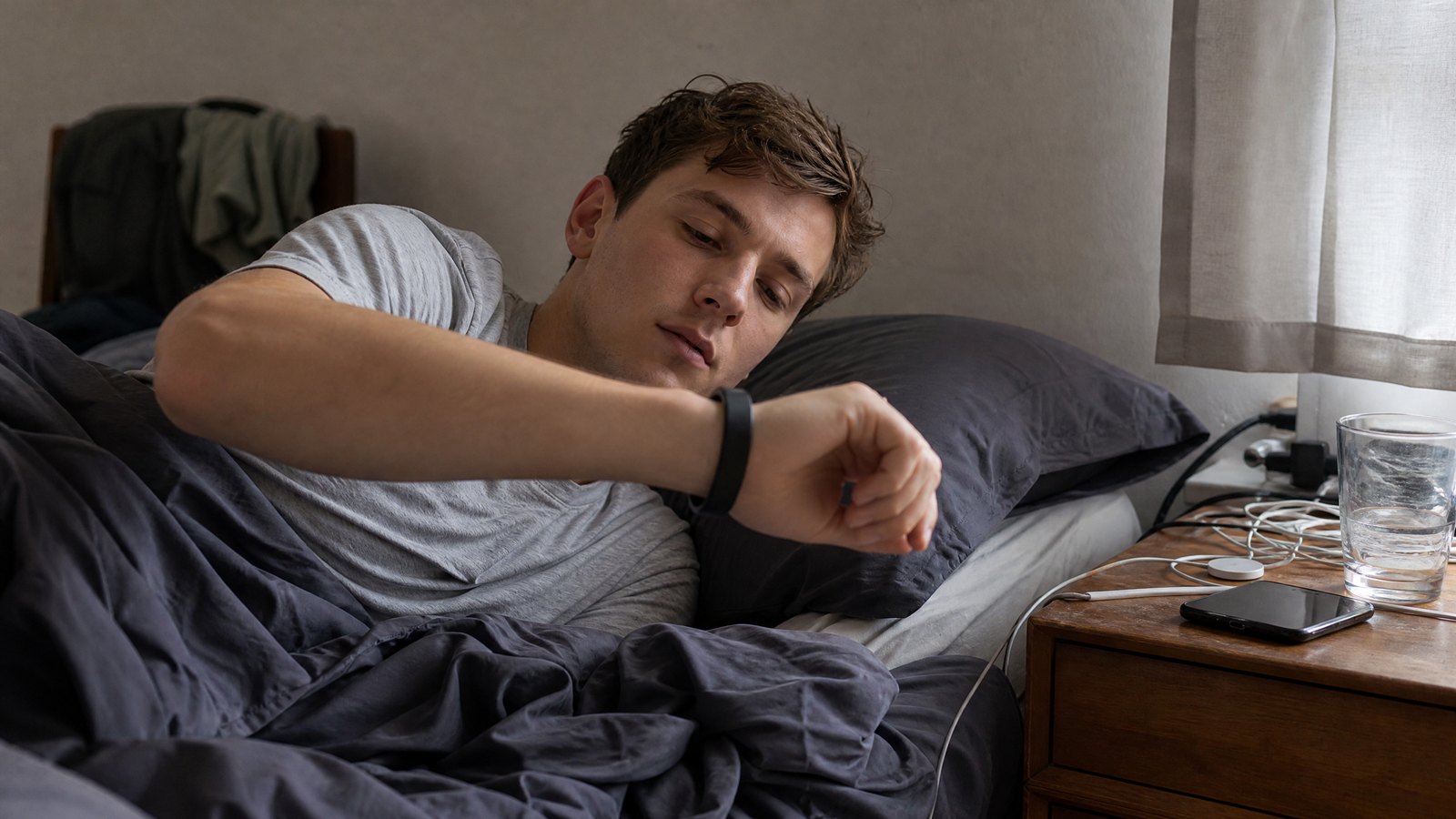 Young adult with ADHD waking to a wearable alarm clock in a calm early-morning bedroom